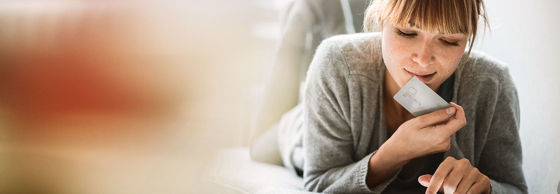 InternetSchutz - Frau liegt mit Kreditkarte und Laptop auf dem Sofa.