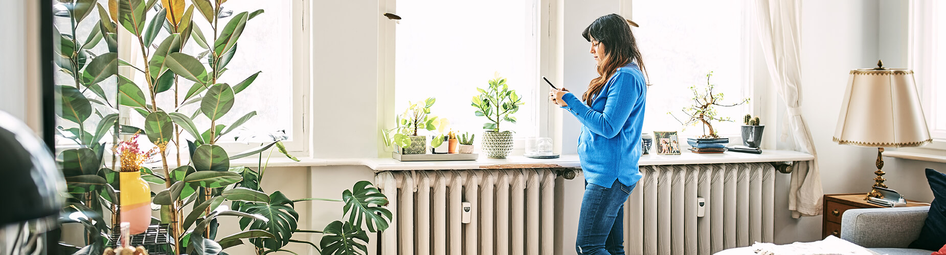 Frau steht in ihrem Wohnzimmer und schaut auf ihr Smartphone